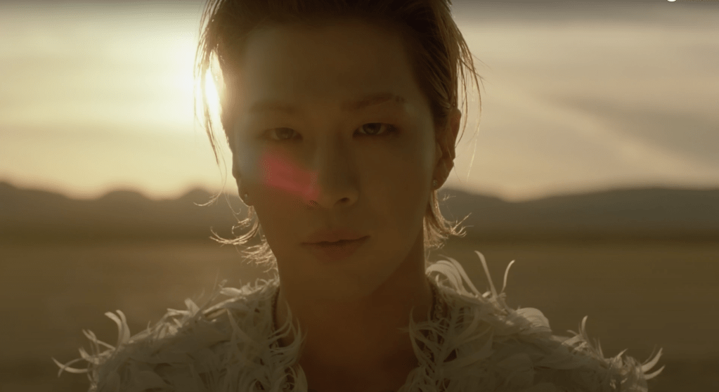 Taeyang com o pôr do sol no fundo em cena do MV de Seed do álbum Down to Earth