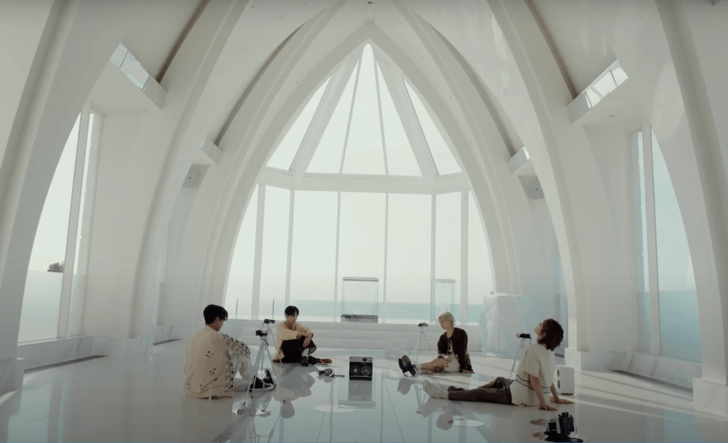 Cena do MV de The Feeling do SHINee com Minho, Taemin, Onew e Key reunidos em um ambient iluminado com câmeras