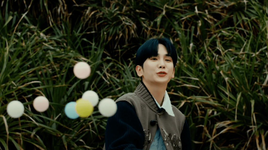Cena do MV de The Feeling do SHINee com Key jogando bolinhas de pingue-pongue e sorrindo