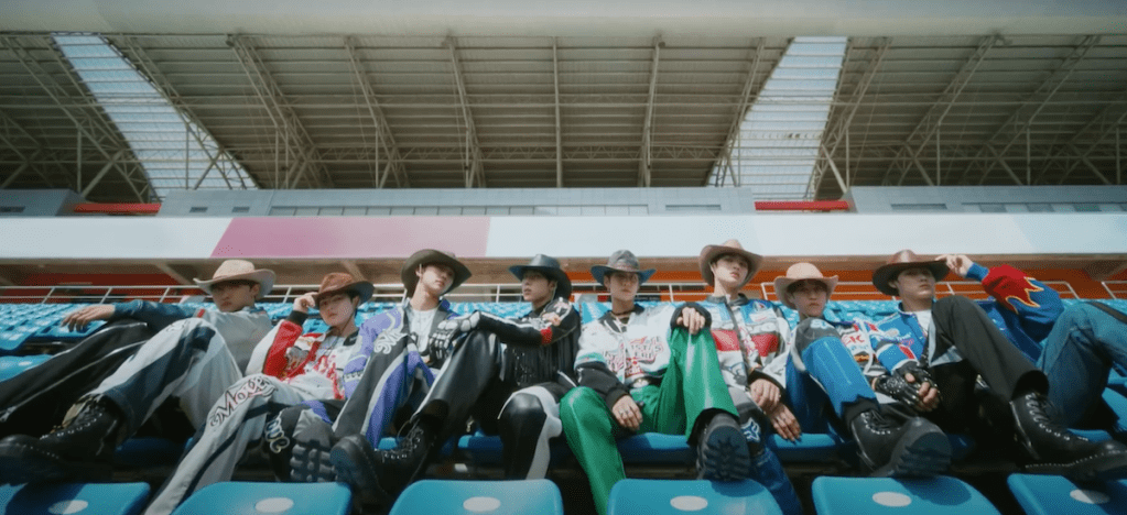 Debut do grupo LUN8 com todos os membros sentados em cadeiras de uma pista de corrida para cena do MV de Wild Heart