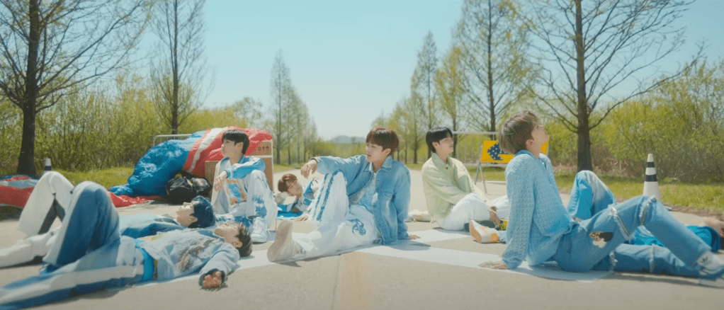 Debut do grupo LUN8 com todos os membros sentados em uma estrada com uma floresta ao fundo em cena do MV de Wild Heart