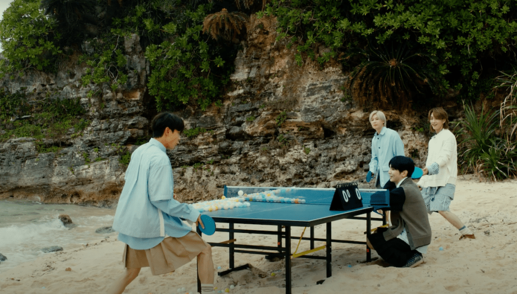 Cena do MV de The Feeling do SHINee com Minho, Taemin, Onew e Key jogando pingue-pongue na praia
