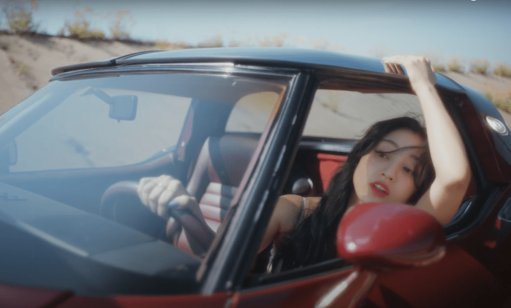 Jihyo dirigindo um carro vermelho em cena do MV de Killin' Me Good do álbum ZONE