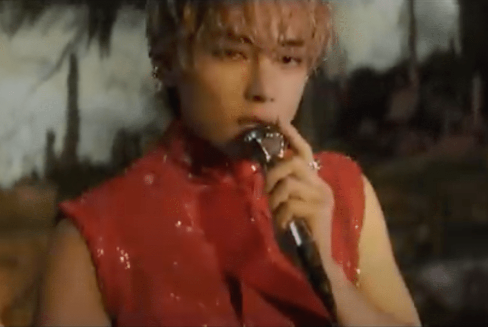 Cena do Kim Taehyung (V do BTS) com microfone nas mãos no MV de "Love Me Again"