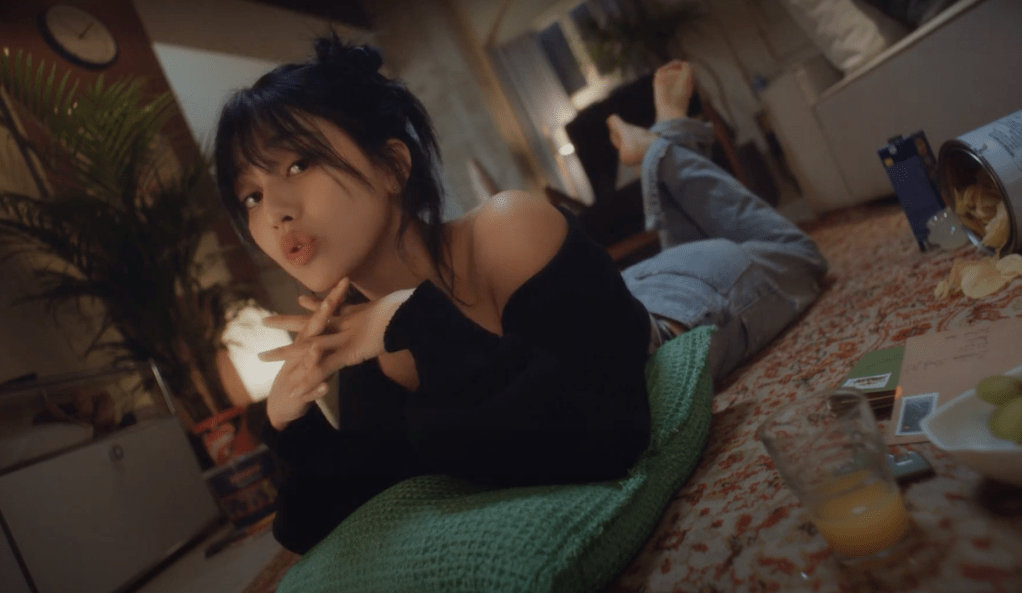 Jihyo deitada no tapete da sala em cena do MV de Killin' Me Good do álbum ZONE