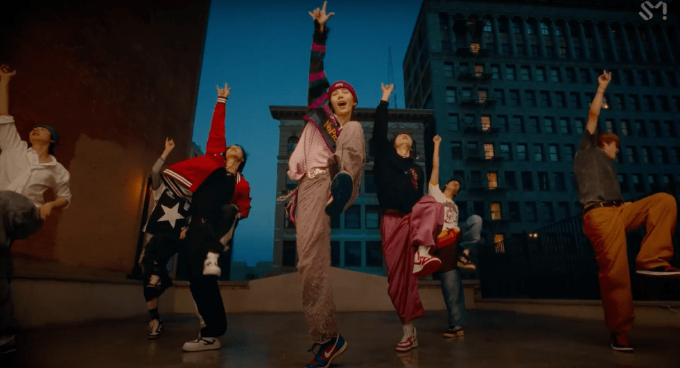 Cena de MV de "Get a Guitar" com os membros do RIIZE dançando ao ar livre cheios de energia, em um cenário noturno