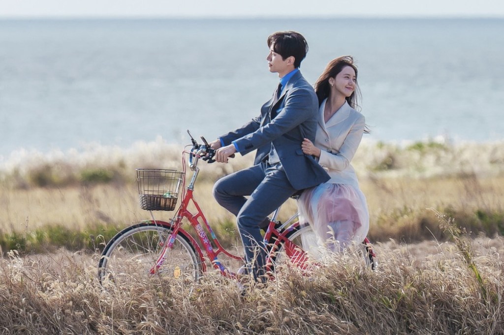 Cena do K-Drama King the Land com Gu Won (Lee Junho) e Sa-Rang (YoonA) andando de bicicleta juntos