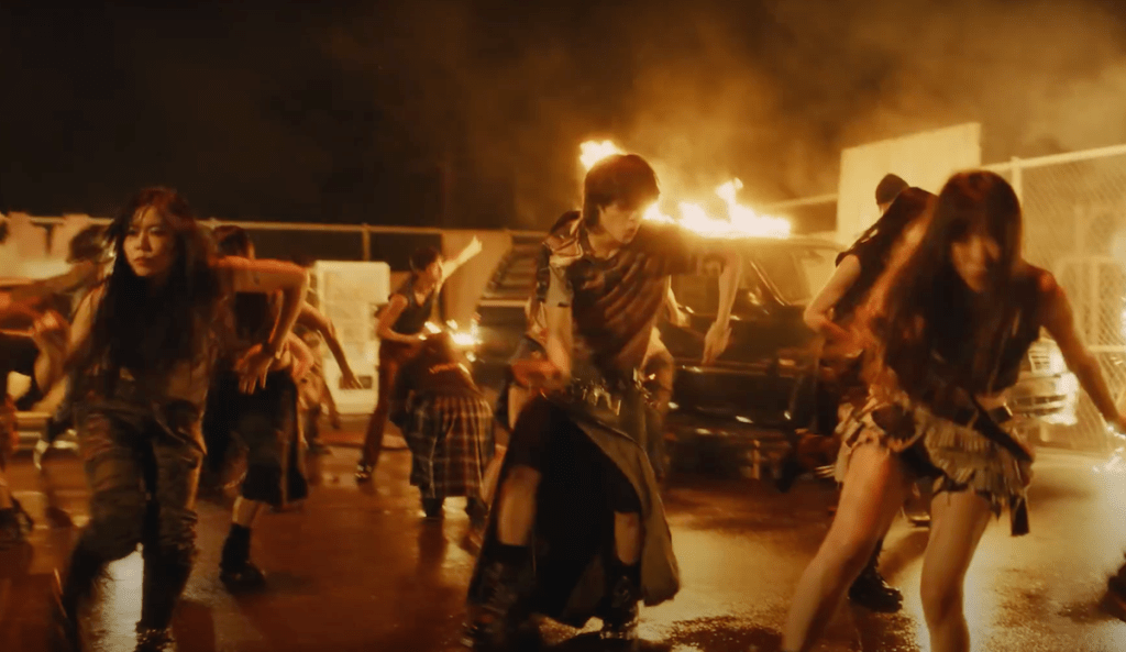 Cena do MV de Guilty com Taemin dançando ao lado dos dançarinos  com fogo no fundo do cenário