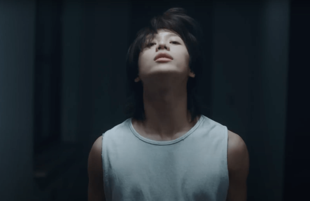 Cena do MV de Guilty com Taemin vestindo uma regata branca em um fundo preto