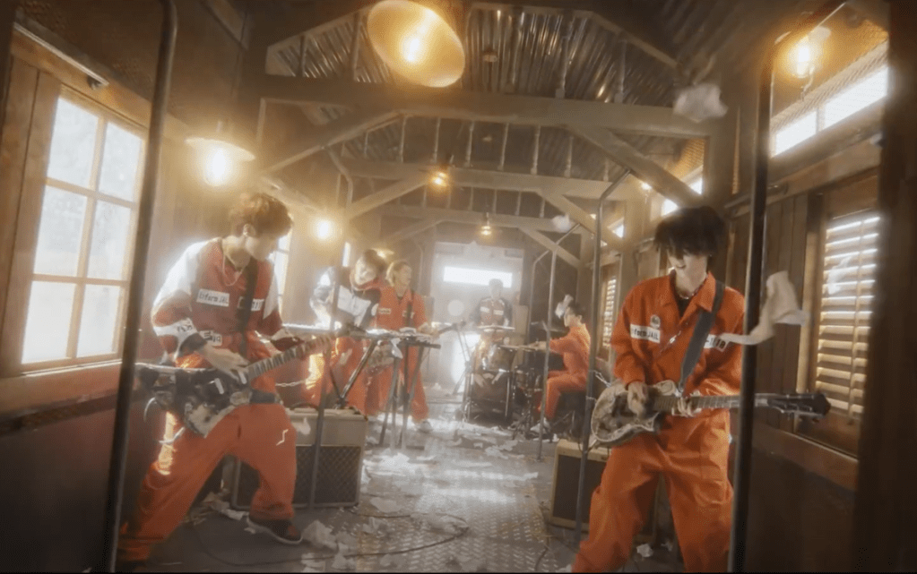 Cena do MV de "Break the Brake" do álbum Livelock com a banda Xdinary Heroes tocando em um vagão de trem