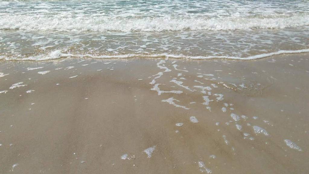 Imagem de uma das praias em Florianópolis mostrando uma pequena onda do mar vindo pela areia 