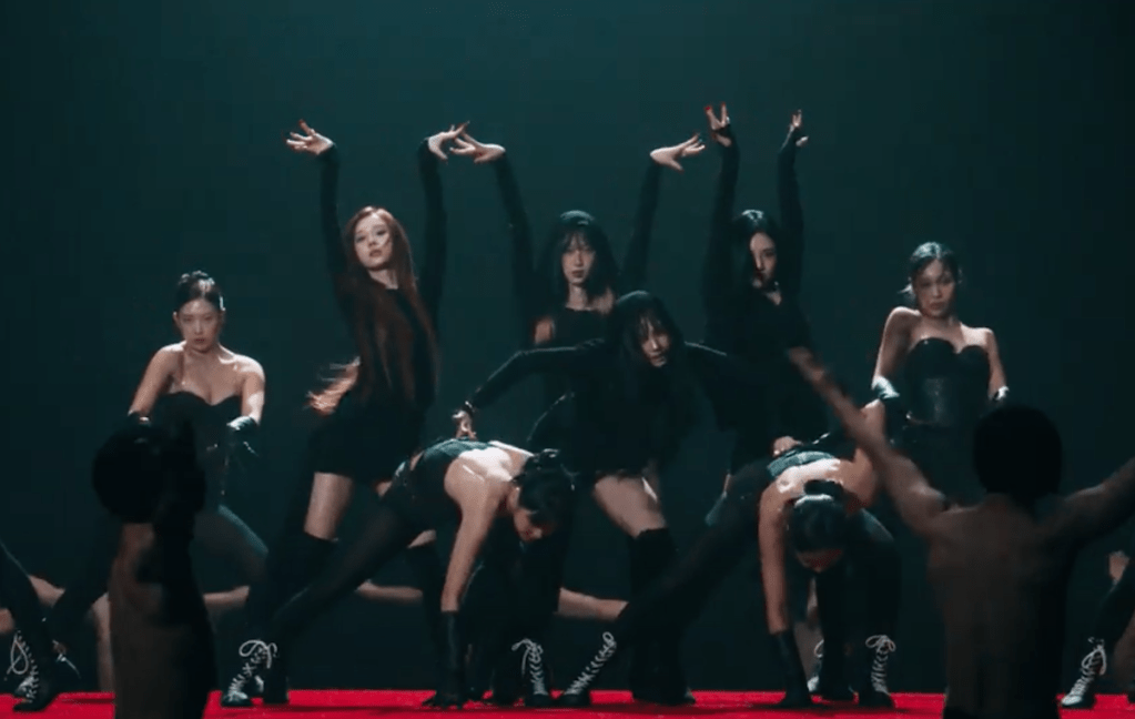 Cena do MV de "Drama", titletrack dio álbum Drama do grupo vespa com Karina, Ningning, Winter e Giselle dançando com roupas pretas