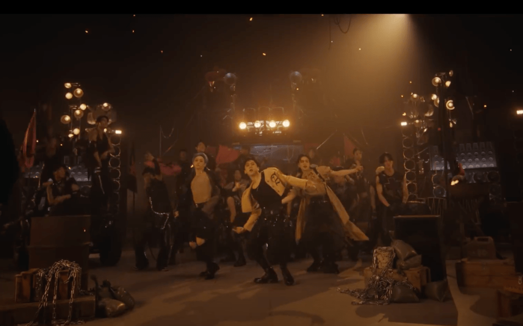 Cena do MV de "LALALA" do álbum 樂-STAR do Stray Kids com os meninos dançando em um cenário escuro iluminado por spotlights