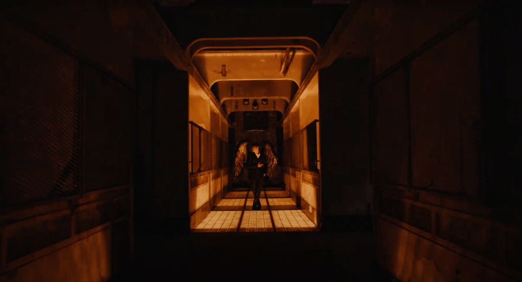 Cena do MV de "Standing Next to You" do album Golden com Jungkook em um túnel com baixa iluminação, usando asas de anjo