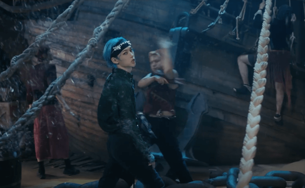 Cena do MV de "LALALA" do álbum 樂-STAR do Stray Kids com Felix em foco e um navio ancorado ao fundo