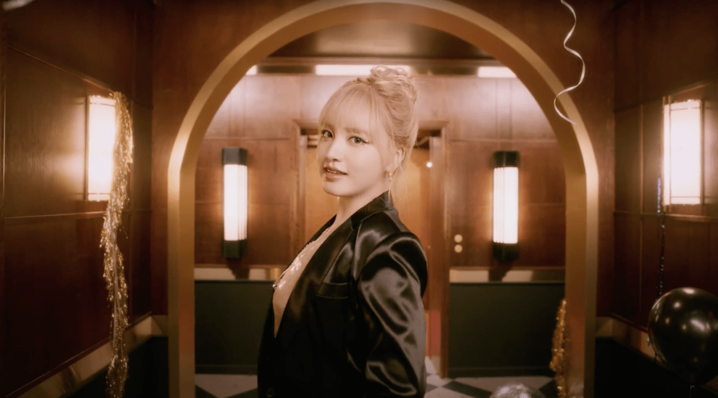 Cena do MV de "Nobody" com Liz do grupo IVE em um corredor com balões de festa