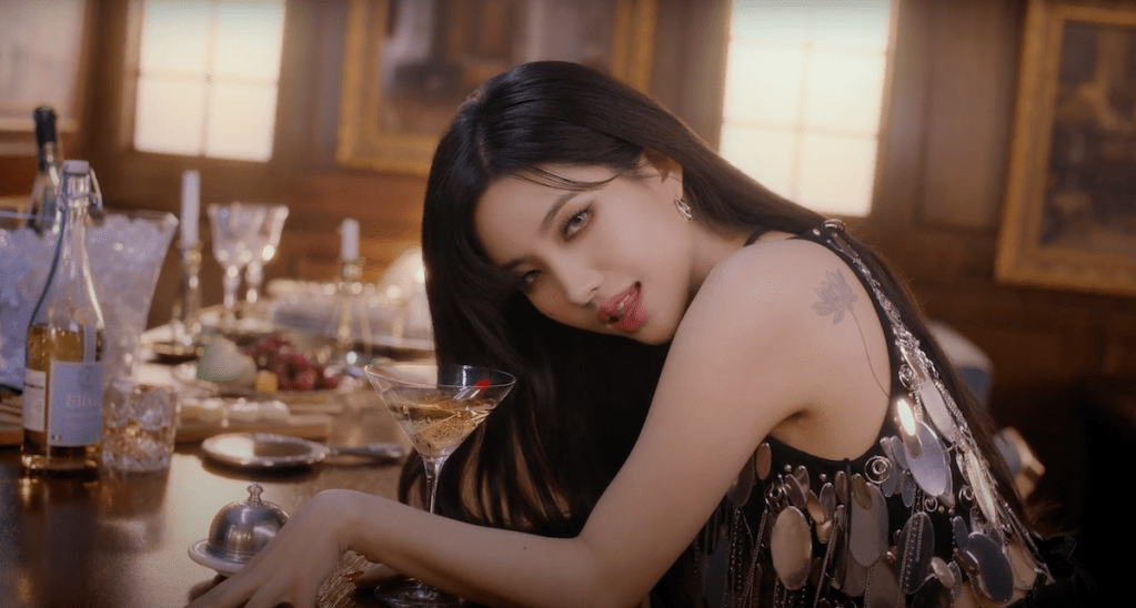Cena do MV de "Nobody" com Soyeon do grupo (G)I-DLE sentada no balcão de um bar