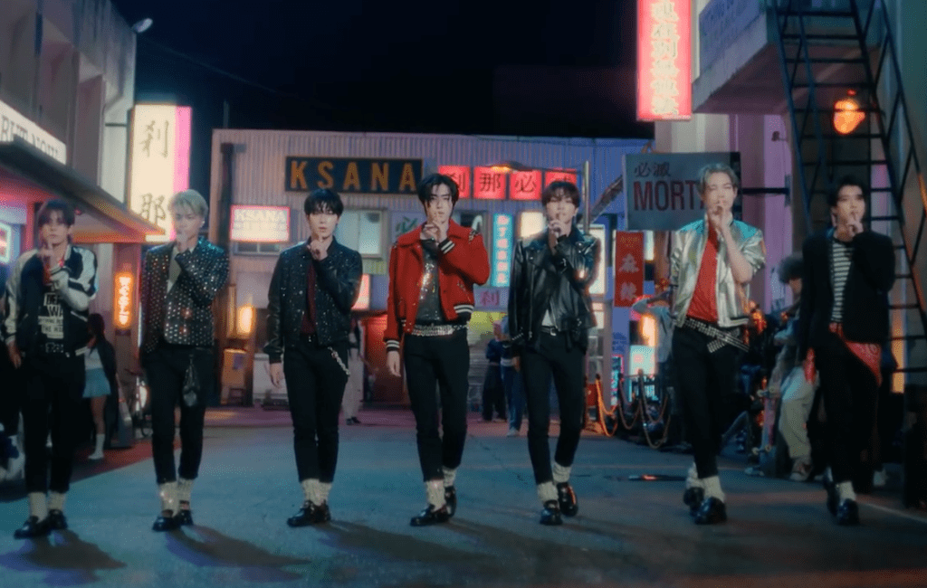 Cena do MV de "Sweet Venom", titletrack do álbum Orange Blood do ENHYPEN com o grupo no centro, em posição de 'shh'