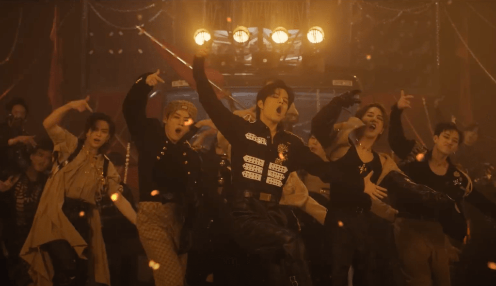 Cena do MV de "LALALA" do álbum 樂-STAR do Stray Kids com os meninos dançando em um cenário escuro iluminado por spotlights