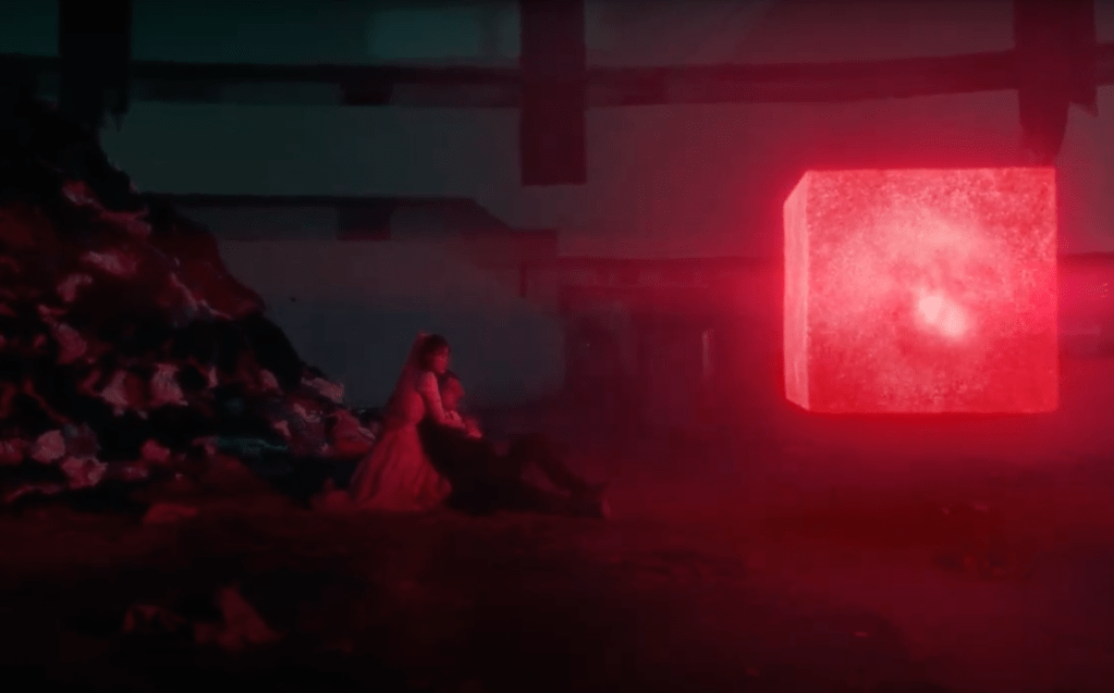 Cena do MV do single "Love wins all" com IU e V olhando para um cubo vermelho flutuante