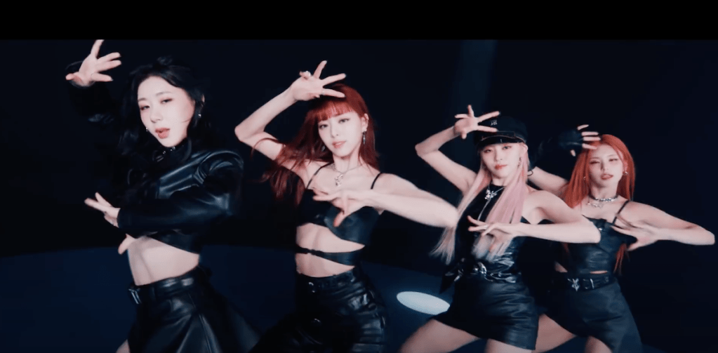 Cena do MV de UNTOUCHABLE do álbum Born to Be com as meninas do Itzy — Chaeryeong, Yuna, Ryujin e Yeji — dançando em um fundo preto enquanto olham para a câmera