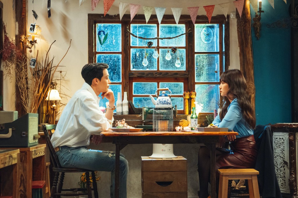 Cena do K-Drama Search: WWW com Mo-Gun olhando para a Ta-Mi, ambos sentados perto da janela em um restaurante