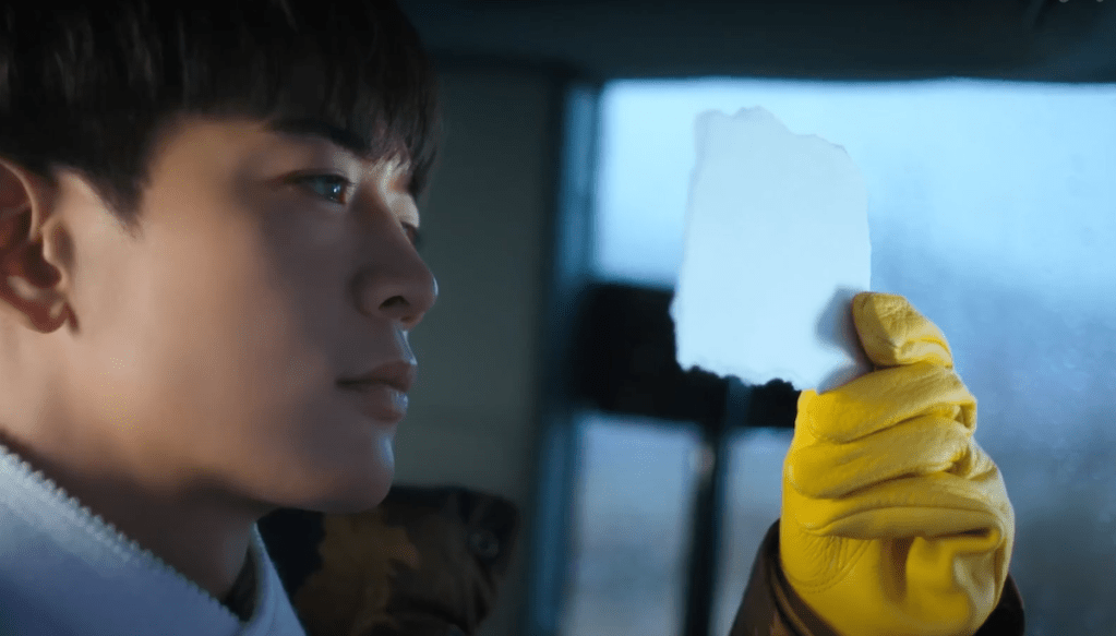 Minho (SHINee) em cena do MV de "Stay For a Night", olhando para um papel branco em suas mãos