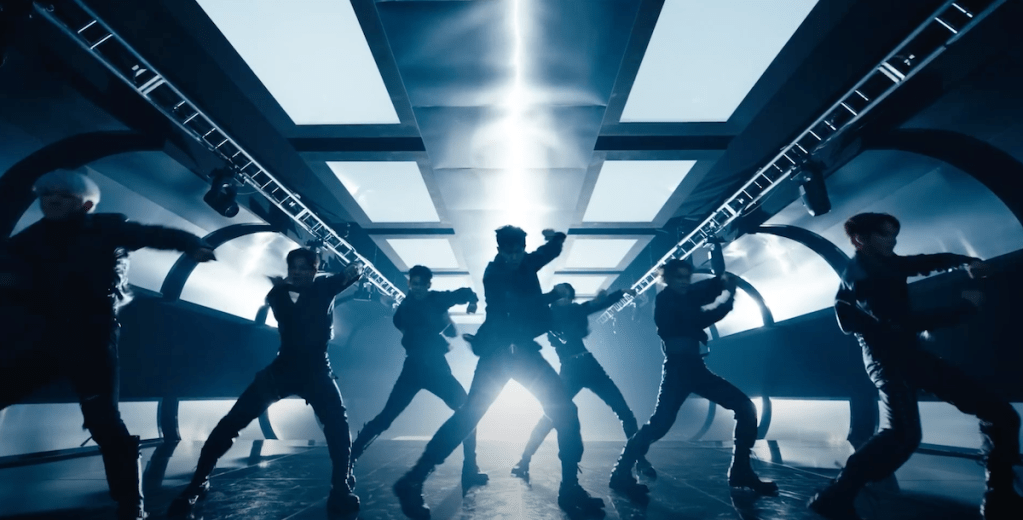 Cena do MV de "UGLY" do álbum Un: SEEN do EVNNE com a silhueta dos seis membros dançando em um cenário monocromático