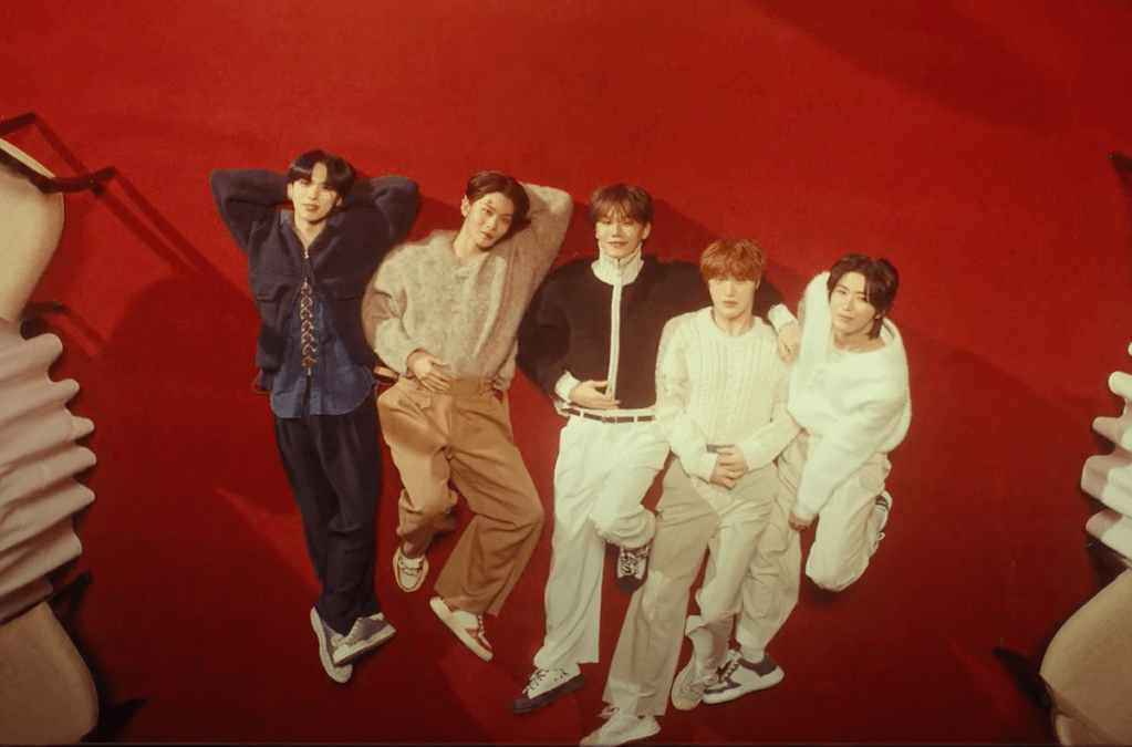 Cena do MV de "Lovers or Enemies" do álbum 0 or 1 do CIX, com os membros deitados em um fundo vermelho, todos olhando para a câmera