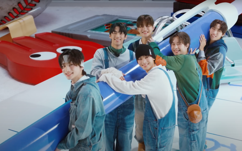 Cena do MV de "plot twist" do album Sparkling Blue com os meninos do TWS segurando um lápis gigante enquanto sorriem para a câmera