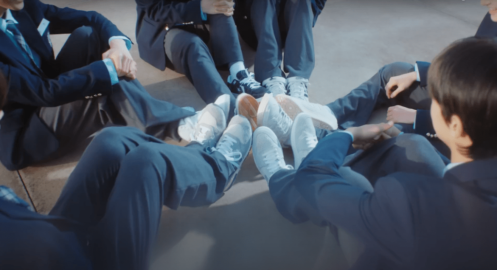 Cena do MV de "plot twist" do album Sparkling Blue com close nos pés dos meninos do TWS juntos formando um círculo