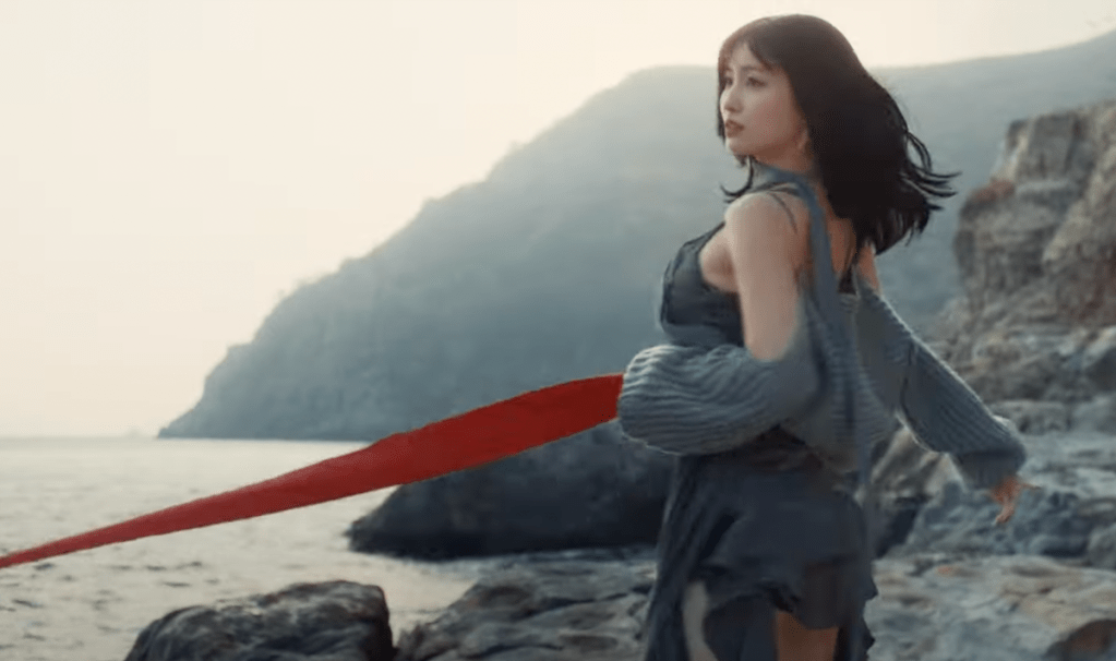 Cena do MV de "I Got You" do TWICE com Momo dançando em um cenário com pedras, montanhas e mar