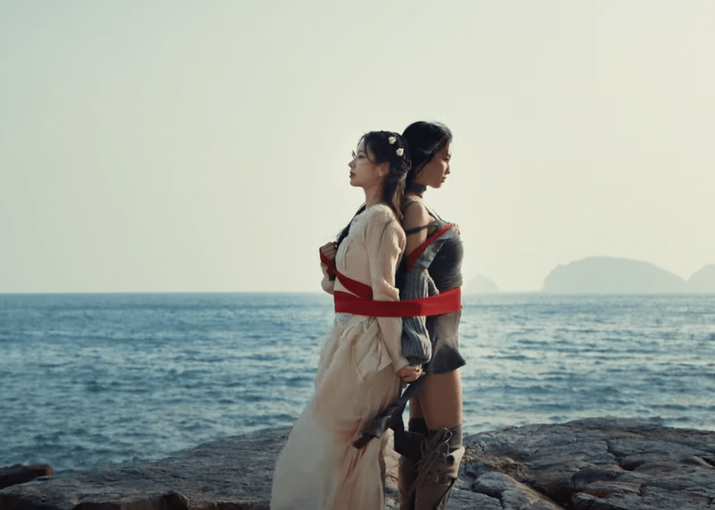 Cena do MV de "I Got You" do TWICE com Momo e Dahyun entrelaçadas por uma fita vermelha e o mar ao fundo