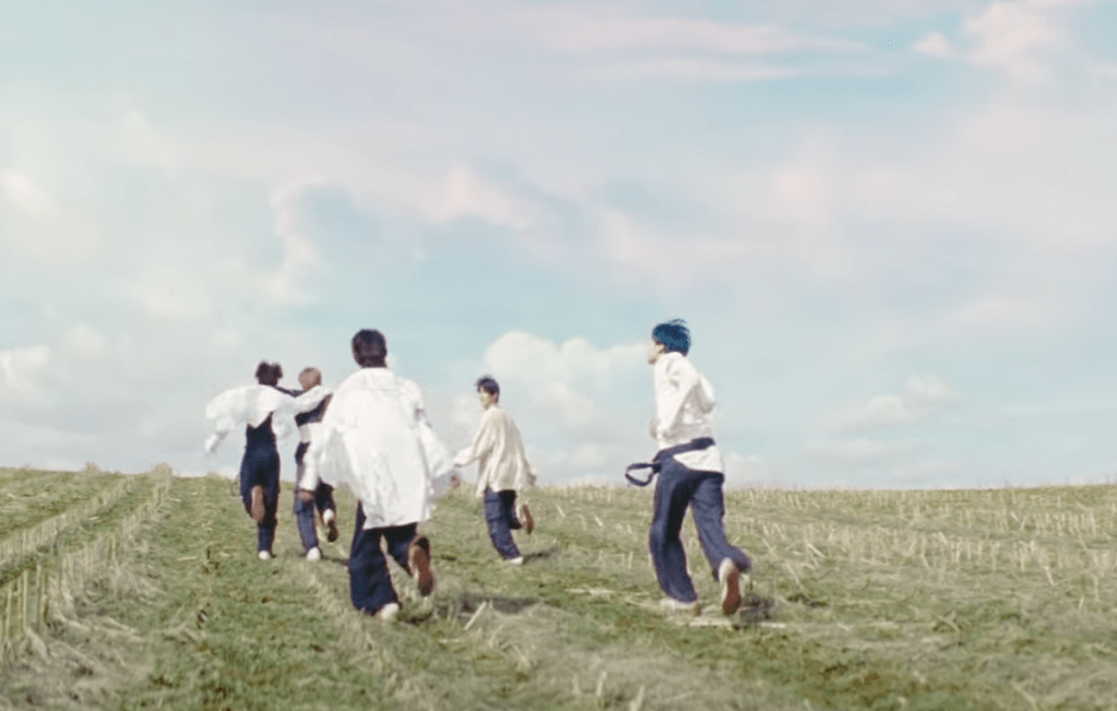 Cena do MV de "Deja Vu", title track do álbum minisode 3: TOMORROW do TXT com todos os membros correndo ao ar livre