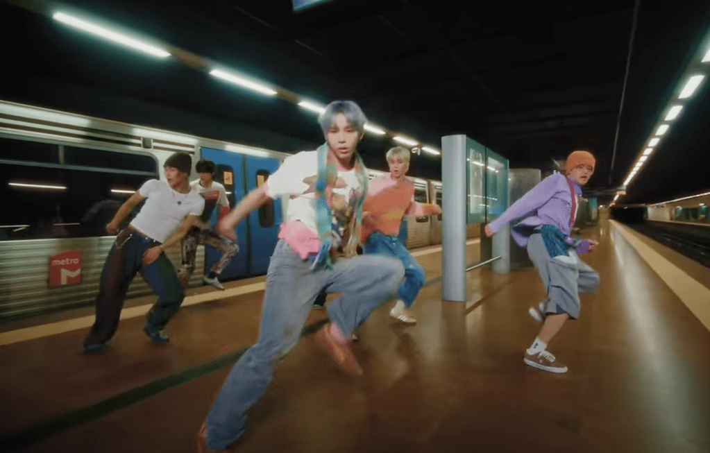 Cena de Anton, Eunseok, Sungchan, Shotaro, Sohee e Wonbin do RIIZE dançando no MV do single "Impossible" em uma estação de metrô