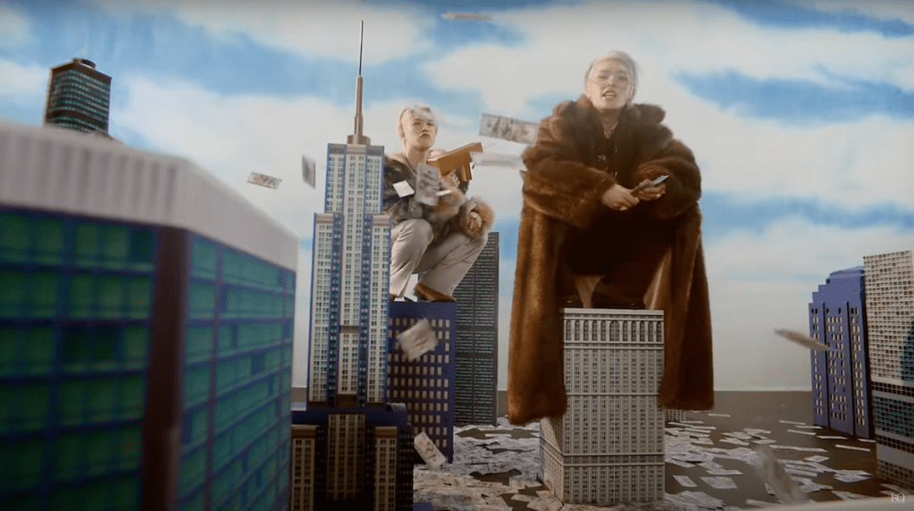 Cena do MV de "WORK" do álbum Golden Hour: Part.1 do ATEEZ com prédios em miniatura e dinheiro caindo do céu