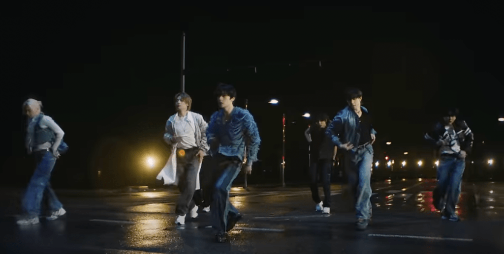 Trecho do MV de "Lose My Breath" do Stray Kids com Charlie Puth em cena noturna no meio da chuva, com os membros dançando 