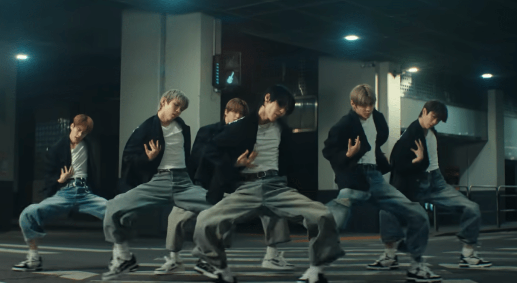 Cena do MV de "Boom Boom Bass" do álbum RIIZING com todos os membros do RIIZE dançando o refrão em um lugar com luz mais baixa e cores frias