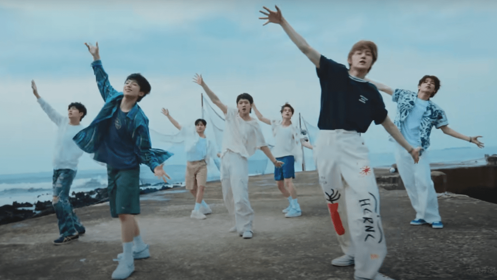 Cena do MV de "Badder Love" do álbum RIDE or DIE com os membros do EVNNE dançando na beira do mar