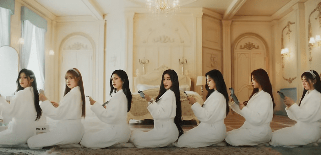 Cena do MV do single "FOREVER" do BABYMONSTER com todas sentadas em fila, usando roupões, em um quarto de hotel