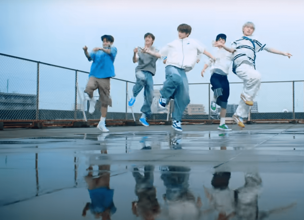 Cena do MV de "If I'm S, Can You Be My N?" do álbum SUMMER BEAT com todos os membros dançando ao ar livre e seus reflexos no chão molhado