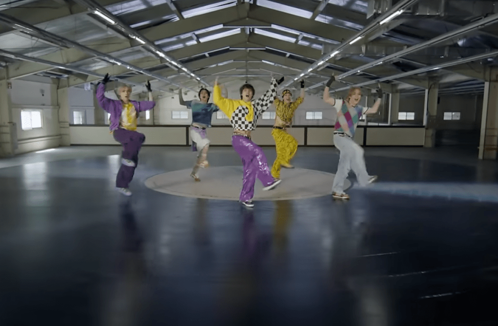 Cena do MV de "Give Me That" com os membros do WayV dançando em cima de um grande disco de vinil