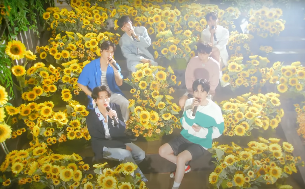Cena do live clip do single "Flower" do INFINITE onde todos os membros cantam rodeados por girassóis