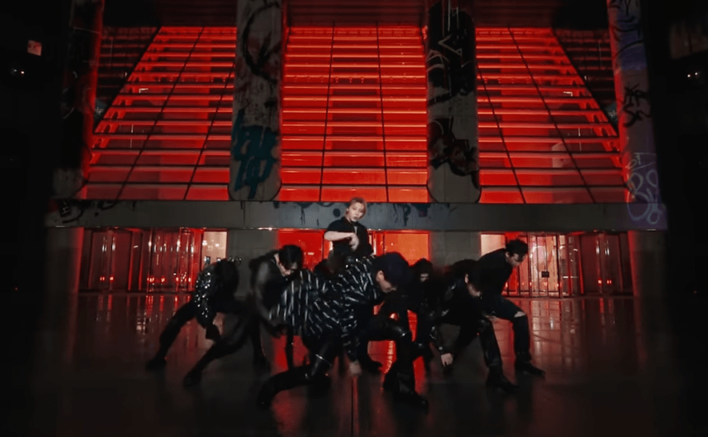 Cena do MV de "Chk Chk Boom" do álbum ATE com todos os membros do Stray Kids dançando em um cenário com fundo vermelho