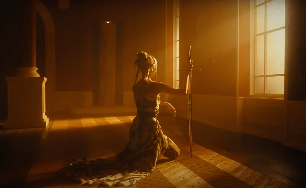 Cena do MV de "JUSTICE" do álbum [VirtuouS] do Dreamcatcher em uma sala iluminada, com os raios de som entrando pela janela e uma das integrantes olhando para fora, ajoelhada e apoiada por uma espada