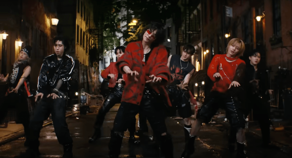 Cena do MV de "Chk Chk Boom" do álbum ATE com todos os membros do Stray Kids dançando ao ar livre durante a noite