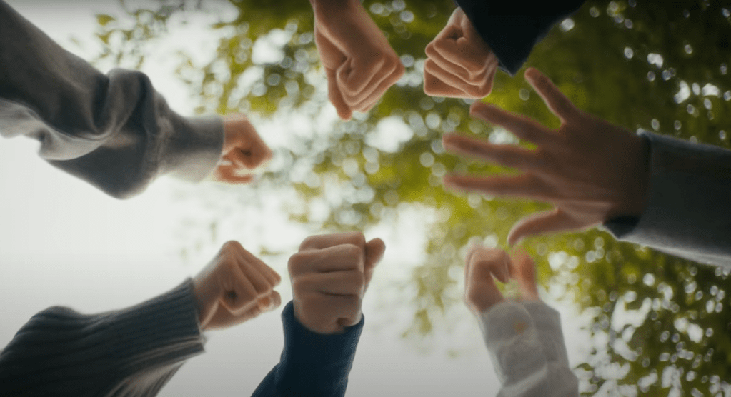 Cena do MV de "XO (Only If You Say Yes)" do álbum ROMANCE : UNTOLD do ENHYPEN com foco nas mãos dos membros jogando 'pedra, papel e tesoura'