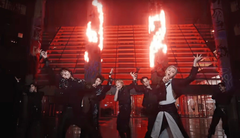 Cena do MV de "Chk Chk Boom" do álbum ATE com todos os membros do Stray Kids dançando em um cenário com fundo vermelho e fogo