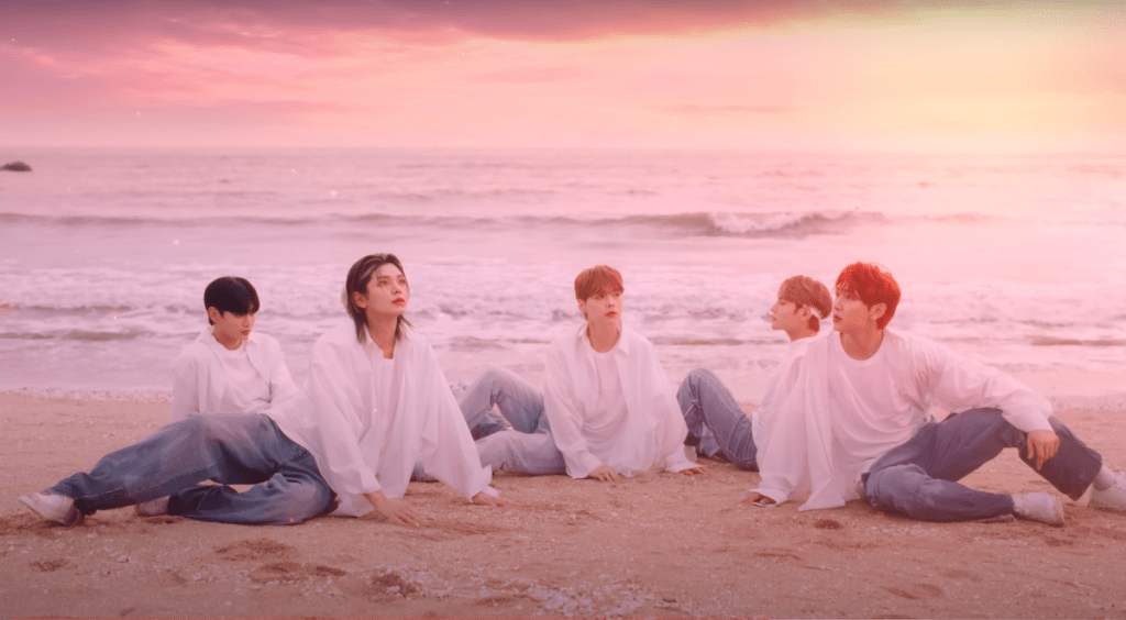 Cena do MV de Vanilla Choco Shake do álbum Sweet Tape do WAKER com todos os membros sentados na areia