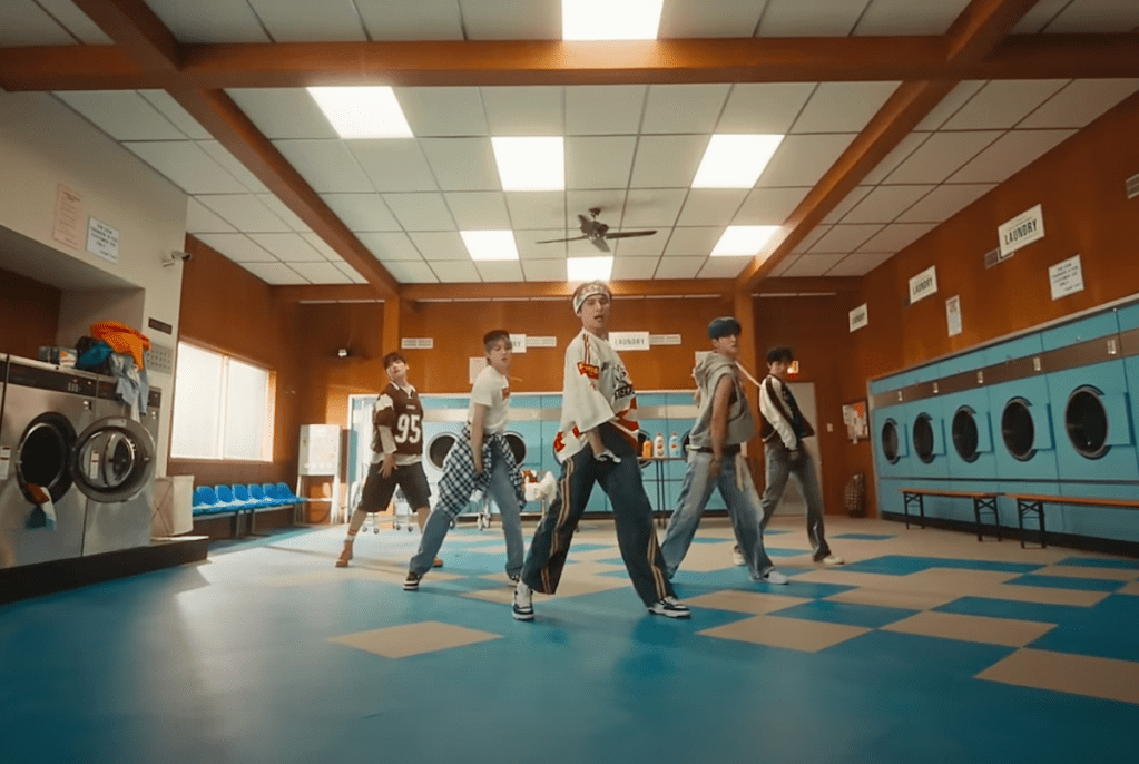 Cena do MV de "Don't Worry, Be Happy" do SF9 com o álbum Fantasy, mostrando Cha Ni, Hwi Young, In Seong, Yoo Tae Yang e Young Bin dançando em um cenário colorido